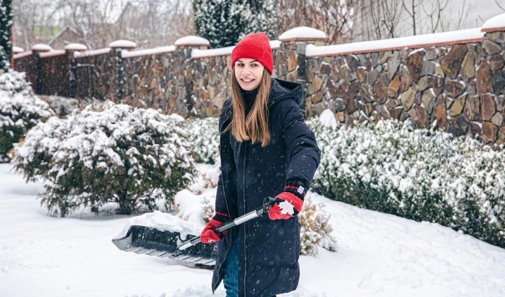 Young woman cleans snow in the yard in snowy weather.
